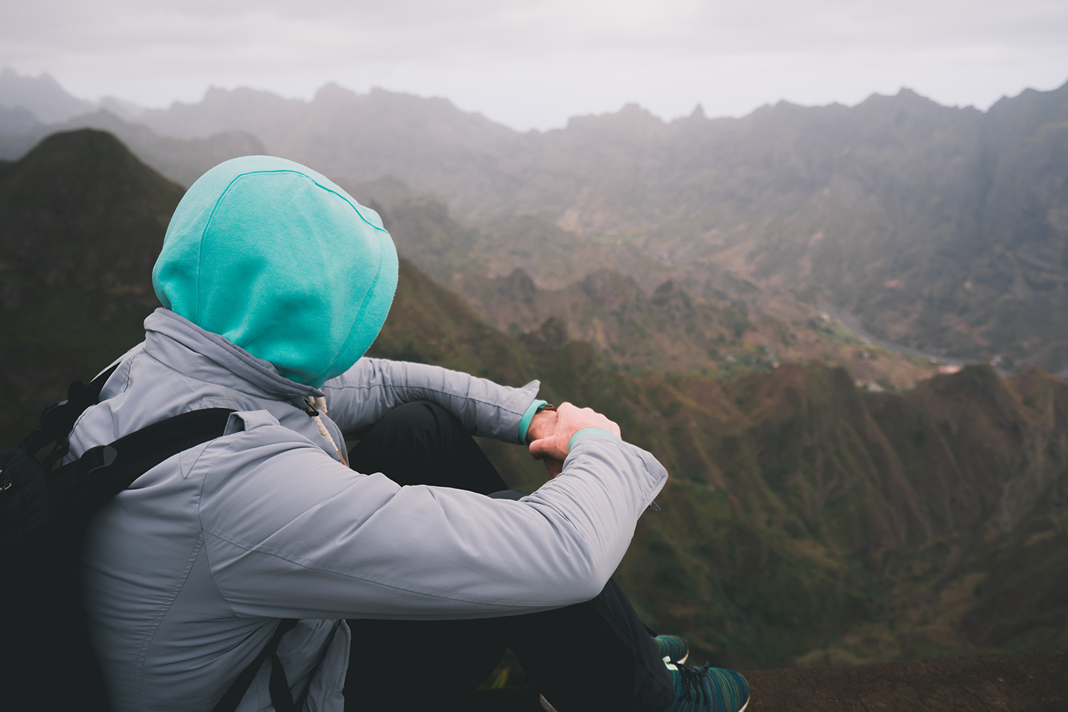 Traveller sitting on a mountain viewpoint with travel clothing and outdoor layers